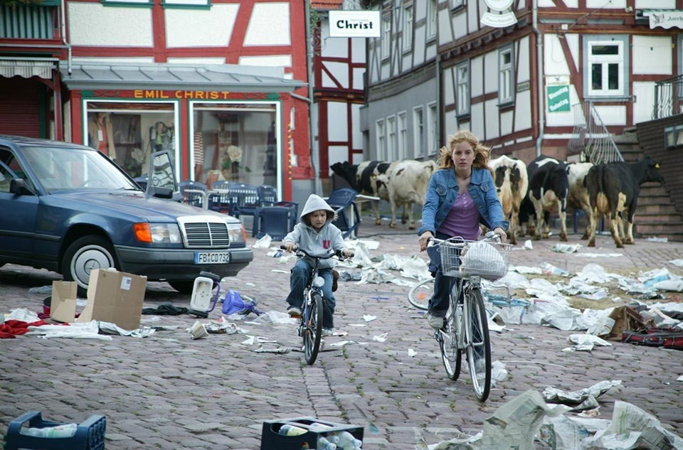 Prizor iz filma Die Wolke (2006). Glavna junakinja in njen bratec se v malem nemškem mestecu prebijata skozi kaos po jedrski katastrofi. Izropana trgovina, opustošenje, v paniki zapuščeni avtomobili, smeti, krave na ulici ...